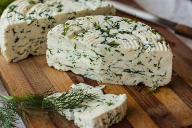 Tahta bir sürahinin yanında baharatlı otlarla ev yapımı organik beyaz peynir dilimlenmiş. Doğal ışık, güzel arkaplan ve tasarımın için yer var.
