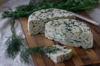 Tahta bir sürahinin yanında baharatlı otlarla ev yapımı organik beyaz peynir dilimlenmiş. Doğal ışık, güzel arkaplan ve tasarımın için yer var.