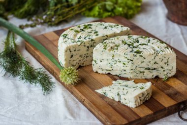 Tahta bir sürahinin yanında baharatlı otlarla ev yapımı organik beyaz peynir dilimlenmiş. Doğal ışık, güzel arkaplan ve tasarımın için yer var.
