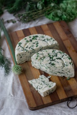 Tahta bir sürahinin yanında baharatlı otlarla ev yapımı organik beyaz peynir dilimlenmiş. Doğal ışık, güzel arkaplan ve tasarımın için yer var.