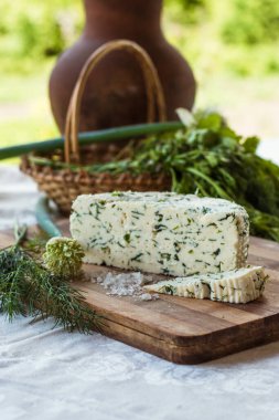 Tahta bir sürahinin yanında baharatlı otlarla ev yapımı organik beyaz peynir dilimlenmiş. Doğal ışık, güzel arkaplan ve tasarımın için yer var.
