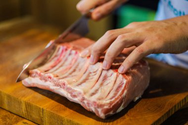 Şef çiğ et keser. Domuz pirzolası doğrayan kasap. Tahta kesme tahtasında kemikli et. Ulusal Mutfak