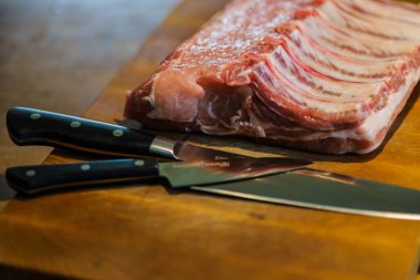 Raw pork ribs on a dark background. Prepared for cutting a large piece on a wooden surface, beautiful knives.