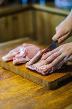 Şef çiğ et keser. Domuz pirzolası doğrayan kasap. Tahta kesme tahtasında kemikli et. Ulusal Mutfak