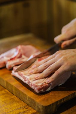 Şef çiğ et keser. Domuz pirzolası doğrayan kasap. Tahta kesme tahtasında kemikli et. Ulusal Mutfak