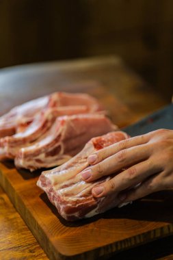 Şef çiğ et keser. Domuz pirzolası doğrayan kasap. Tahta kesme tahtasında kemikli et. Ulusal Mutfak