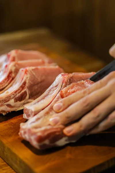 The chef cuts raw meat. Butcher cutting pork ribs. Meat with bone on a wooden cutting board. National cuisine