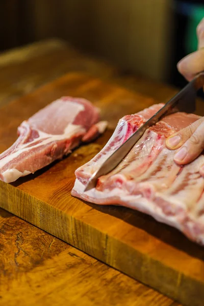 The chef cuts raw meat. Butcher cutting pork ribs. Meat with bone on a wooden cutting board. National cuisine