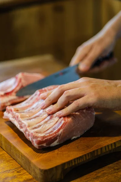 The chef cuts raw meat. Butcher cutting pork ribs. Meat with bone on a wooden cutting board. National cuisine