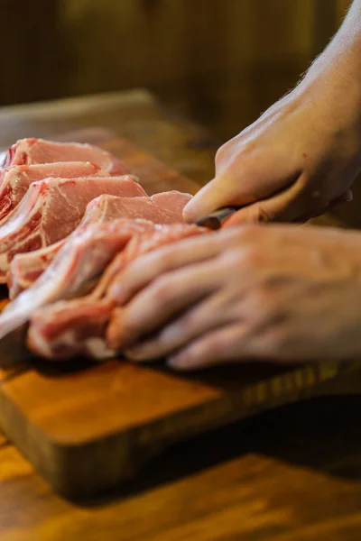 The chef cuts raw meat. Butcher cutting pork ribs. Meat with bone on a wooden cutting board. National cuisine