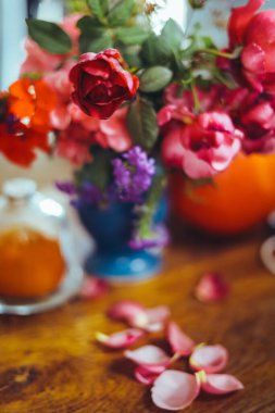 Bir buket parlak gül çiçeği, masasında mavi bir vazoda sardunyalar, bir portakal, yapraklar. Doğal ışık, yakın çekim, güzel arkaplan, dokular.