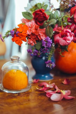 Bir buket parlak gül çiçeği, masasında mavi bir vazoda sardunyalar, bir portakal, yapraklar. Doğal ışık, yakın çekim, güzel arkaplan, dokular.