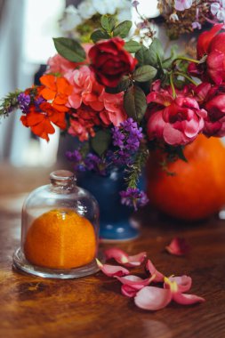 Bir buket parlak gül çiçeği, masasında mavi bir vazoda sardunyalar, bir portakal, yapraklar. Doğal ışık, yakın çekim, güzel arkaplan, dokular.