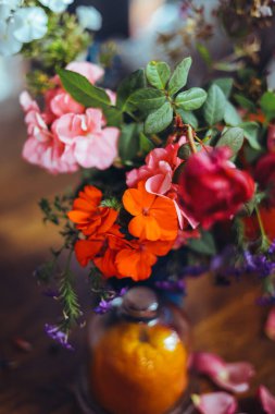 Bir buket parlak gül çiçeği, masasında mavi bir vazoda sardunyalar, bir portakal, yapraklar. Doğal ışık, yakın çekim, güzel arkaplan, dokular.