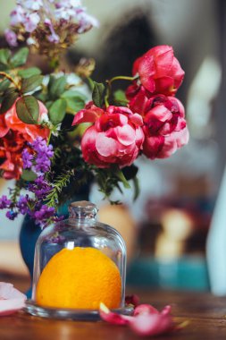 Bir buket parlak gül çiçeği, masasında mavi bir vazoda sardunyalar, bir portakal, yapraklar. Doğal ışık, yakın çekim, güzel arkaplan, dokular.