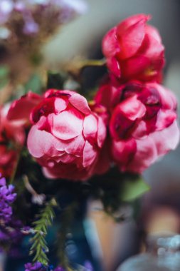 Bir buket parlak gül çiçeği, masasında mavi bir vazoda sardunyalar, bir portakal, yapraklar. Doğal ışık, yakın çekim, güzel arkaplan, dokular.