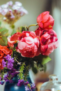 Bir buket parlak gül çiçeği, masasında mavi bir vazoda sardunyalar, bir portakal, yapraklar. Doğal ışık, yakın çekim, güzel arkaplan, dokular.