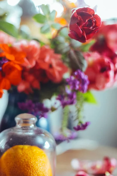 bouquet of bright rose flowers, geraniums in a blue vase on the table, an orange, petals. natural light, close-up, beautiful background, textures.