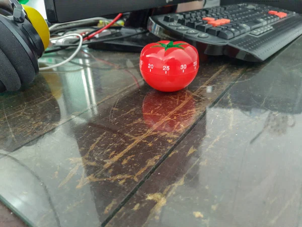 木のテーブルの上に置かれた赤いトマトの形をしたポモドーロキッチンタイマー 周りのカラフルなオブジェクト — ストック写真
