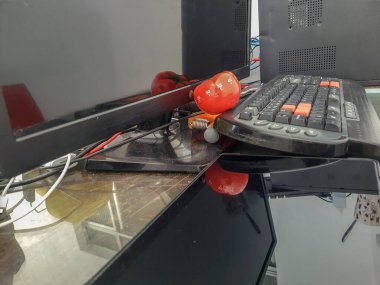 Pomodoro mutfak zamanlayıcısı ahşap bir masanın üzerinde duran kırmızı domates şeklinde ve etrafında renkli nesneler var.