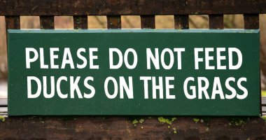 Please Do Not Feed Ducks On The Grass - wooden sign on bench background banner image