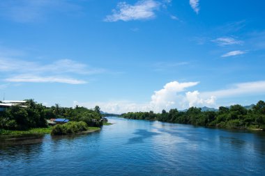 Yeşil sahilli geniş nehir ve bulutlu gökyüzü.