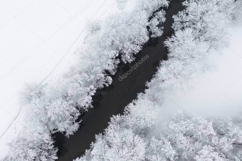 Aerial view of snowy trees and a little curvy winding stream.  Christmas, winter time, first snow