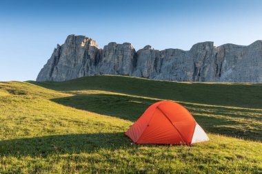 A glowing tent in the mountains under a blue morning sky. Sunrise and mountains in the background. Summer landscape. Panorama Bright tourist tent in the mountains nature.