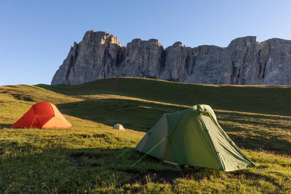 A glowing tent in the mountains under a blue morning sky. Sunrise and mountains in the background. Summer landscape. Panorama Bright tourist tent in the mountains nature.