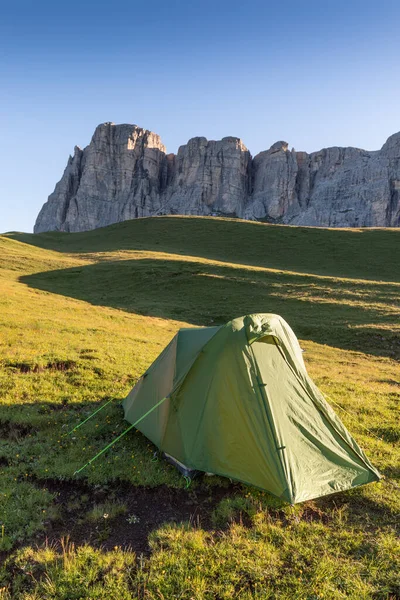 A glowing tent in the mountains under a blue morning sky. Sunrise and mountains in the background. Summer landscape. Panorama Bright tourist tent in the mountains nature.