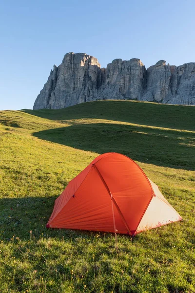 A glowing tent in the mountains under a blue morning sky. Sunrise and mountains in the background. Summer landscape. Panorama Bright tourist tent in the mountains nature.