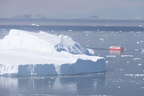 Small ship cruising among ice bergs during beautiful summer day. Disko Bay, Greenland. Climate change and global warming.