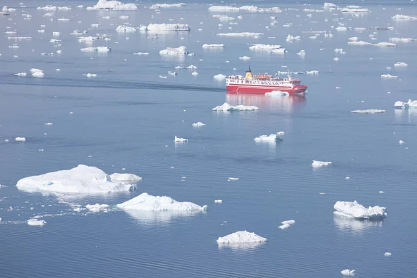 Small ship cruising among ice bergs during beautiful summer day. Disko Bay, Greenland. Climate change and global warming.