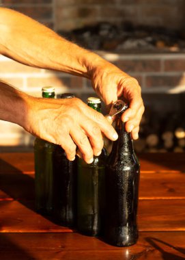 Erkek eller bir şişe bira açar. Mutlu saat, altın gün batımı ışığı verandayı aydınlatıyor..