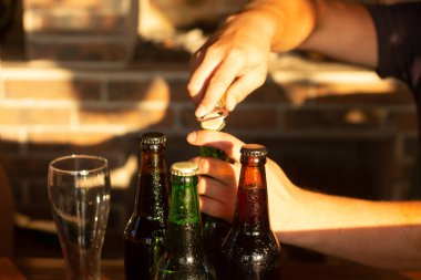 Erkek eller bir şişe bira açar. Mutlu saat, altın gün batımı ışığı verandayı aydınlatıyor..