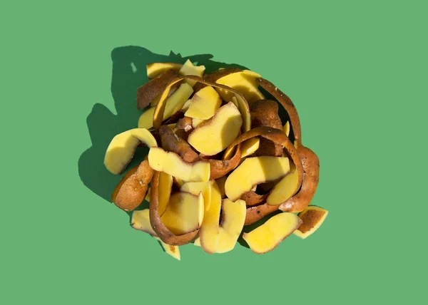 Concept of Stop food waste day. Potato peels are one of the most commonly discarded items during food prep. Green background.