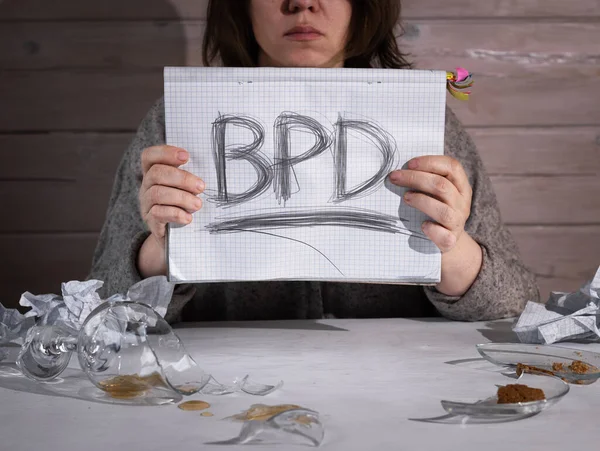 Concept of borderline personality disorder. The abbreviation for BPD is expressively written in pencil with strong pressure on paper. There is crumpled paper and a broken glass on the table. Strong emotional experience.