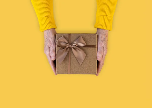 黄色のセーターを着た年配の女性の手には リボンで結ばれたギフトボックスがあります 高齢者の概念の日 トップビュー コピースペース — ストック写真
