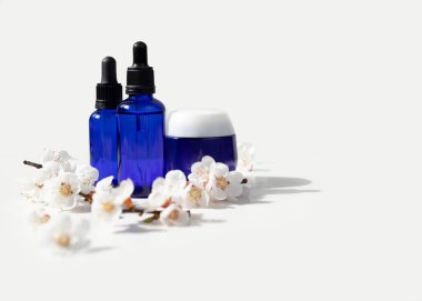 Siyah kapaklı mavi cam damlalar ve beyaz üzerine kiraz çiçekli dallar. Doğal bahar arkaplanı. Organik, biyolojik, doğal kozmetik. Güzellik, cilt bakımı, model..