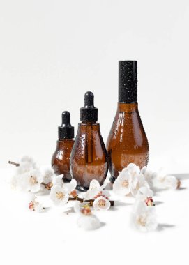 Siyah kapaklı ve beyaz üzerine kiraz çiçeği olan kehribar rengi cam damlalar. Doğal bahar arkaplanı. Organik, biyolojik, doğal kozmetik. Güzellik, cilt bakımı, model..