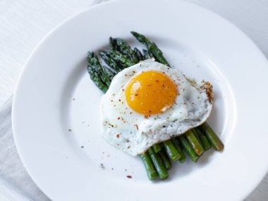 Cooking asparagus. Fried green asparagus sprouts and fried eggs on a white plate. Healthy food and diet.