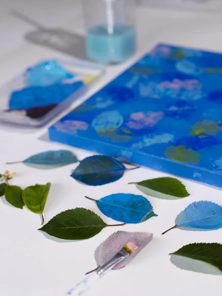 DIY Abstract botanical art. The picture is made by applying acrylic paints on the leaves and stamping on canvas. Blue on blue.