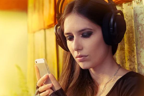 Menina com fones de ouvido grandes e telefone inteligente no fundo Grunge — Fotografia de Stock