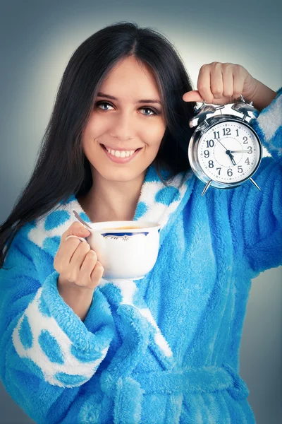 Молодая женщина в халате держит будильник и чашку кофе — стоковое фото