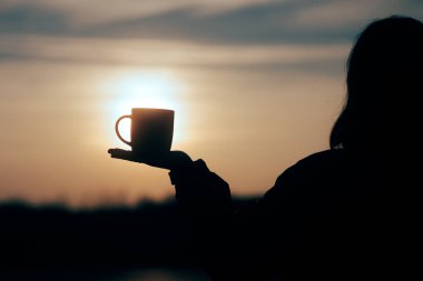 The Sunrise 'da elinde kahve fincanı tutan bir kadının silueti.