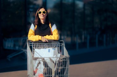 Güneş gözlüğü takan neşeli kadın alışveriş arabasını itiyor.