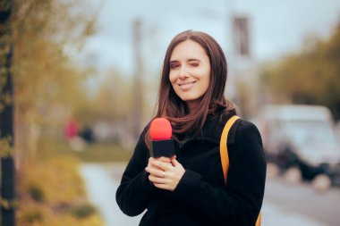  Muhabir elinde mikrofonla caddede işini yapıyor.