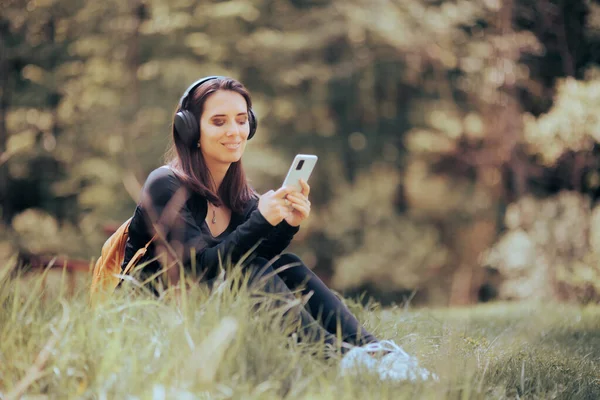 Happy Woman Wearing Headphones Listening to Music Outdoors. Young person relaxing outside in nature wearing wireless headset