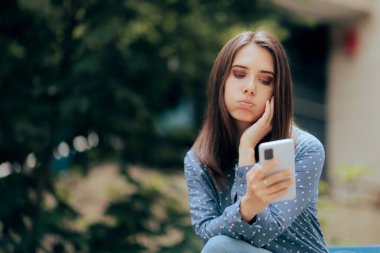 Hayal kırıklığına uğramış bir kadın bankta oturmuş telefonunu kontrol ediyor.