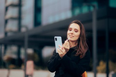 Woman Using Smartphone to Check her Lip Gloss Application 